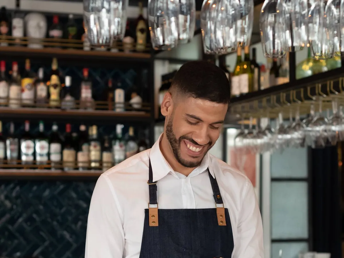 Un serveur souriant ouvre une bouteille derrière le comptoir d'un restaurant